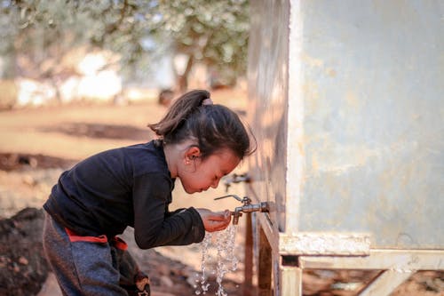 A Cute Little Kid Washing Her Face on the Faucet