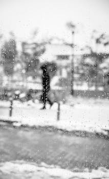 A blurry silhouette walking past a window covered in raindrops on a snowy day.