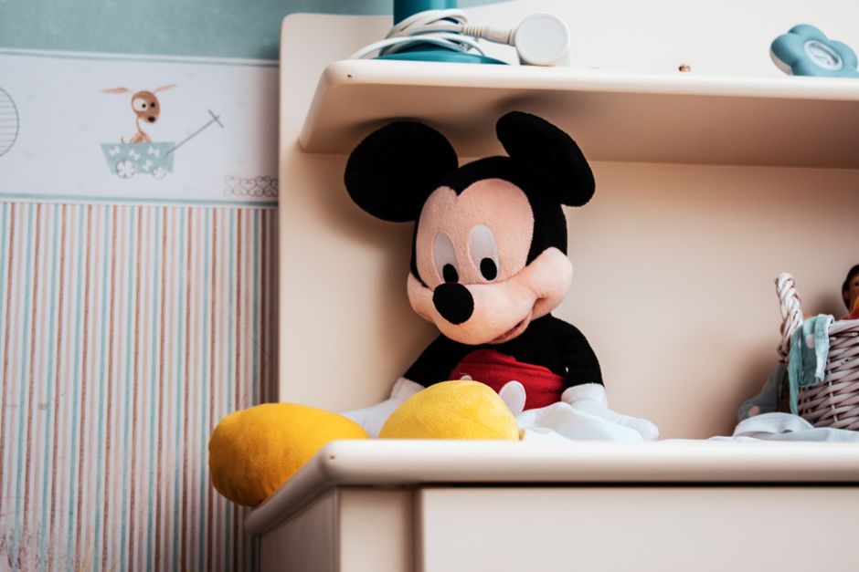 A Mickey Mouse stuffed toy sits on a shelf in a colorful child's room setting.