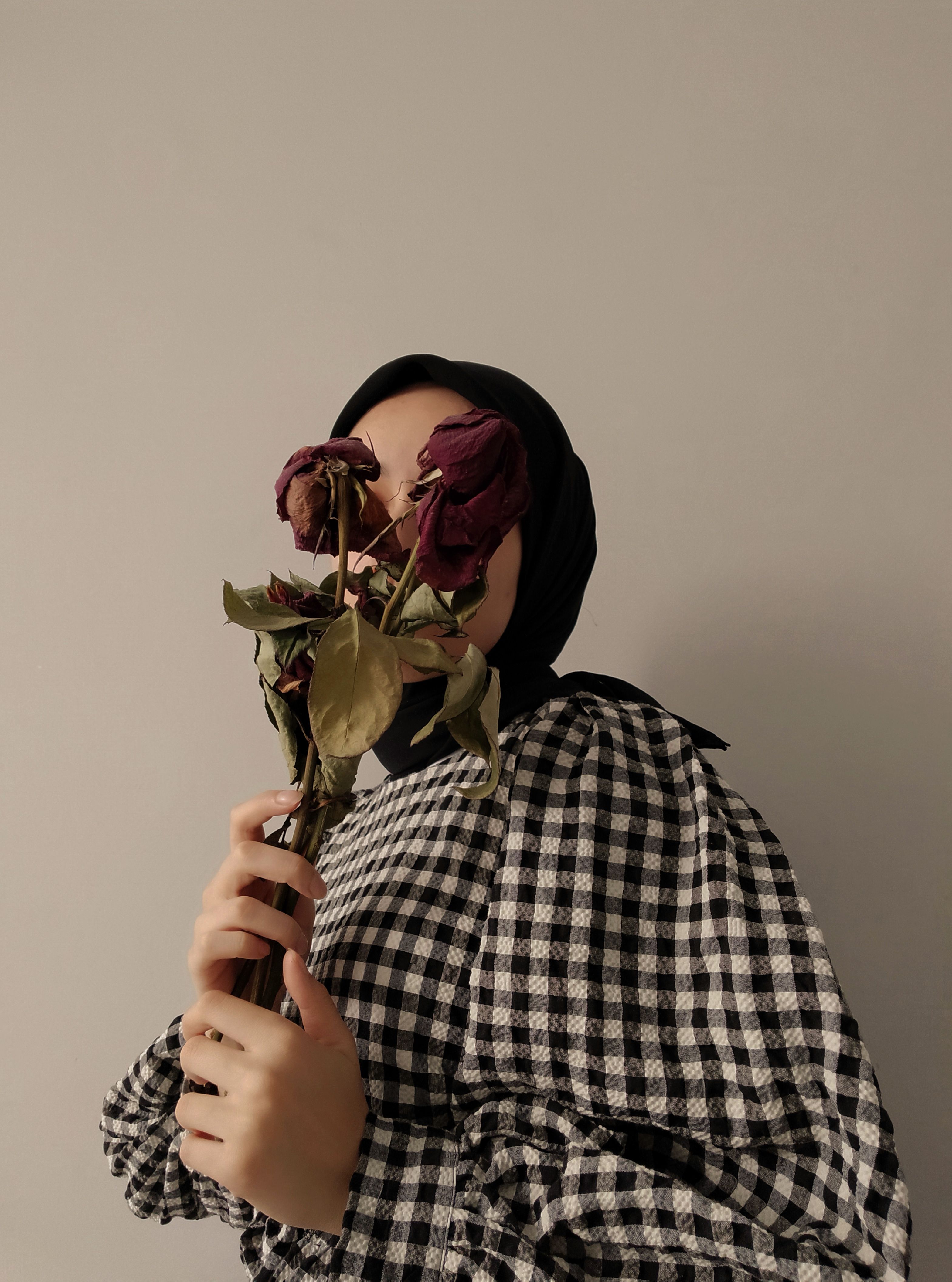A woman in checkered attire holds dried roses, creating a moody floral portrait.