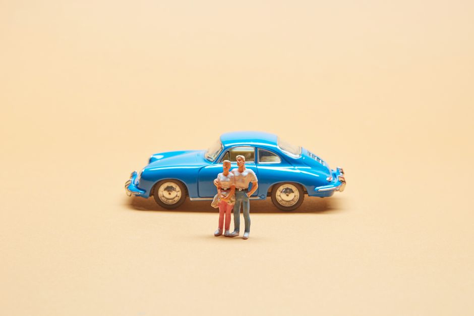 How Gap Insurance Covers Totaled Leased Cars and When You Need It A miniature family standing in front of a classic blue toy car on a beige background, representing family travel concepts.