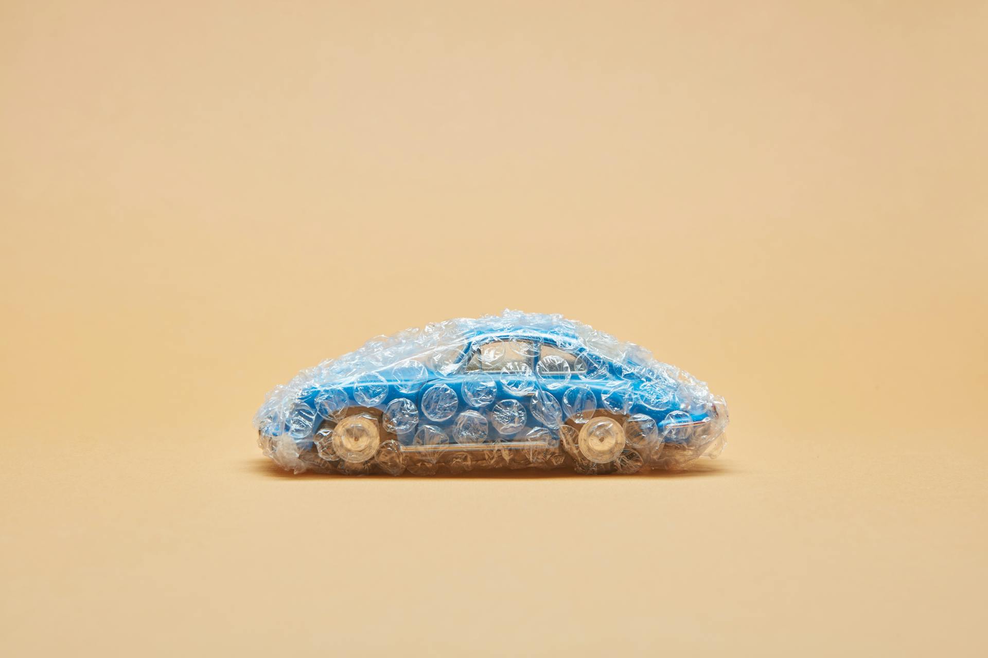 Blue toy car wrapped in bubble wrap against a beige background, minimalist concept.