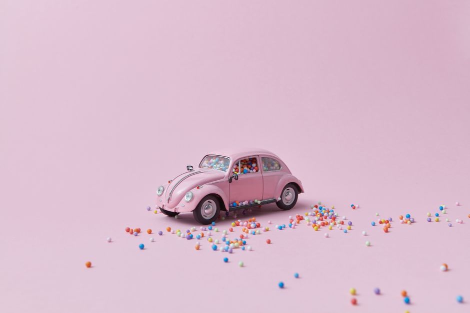 A pink toy Volkswagen Beetle filled with colorful beads on a pastel pink background.
