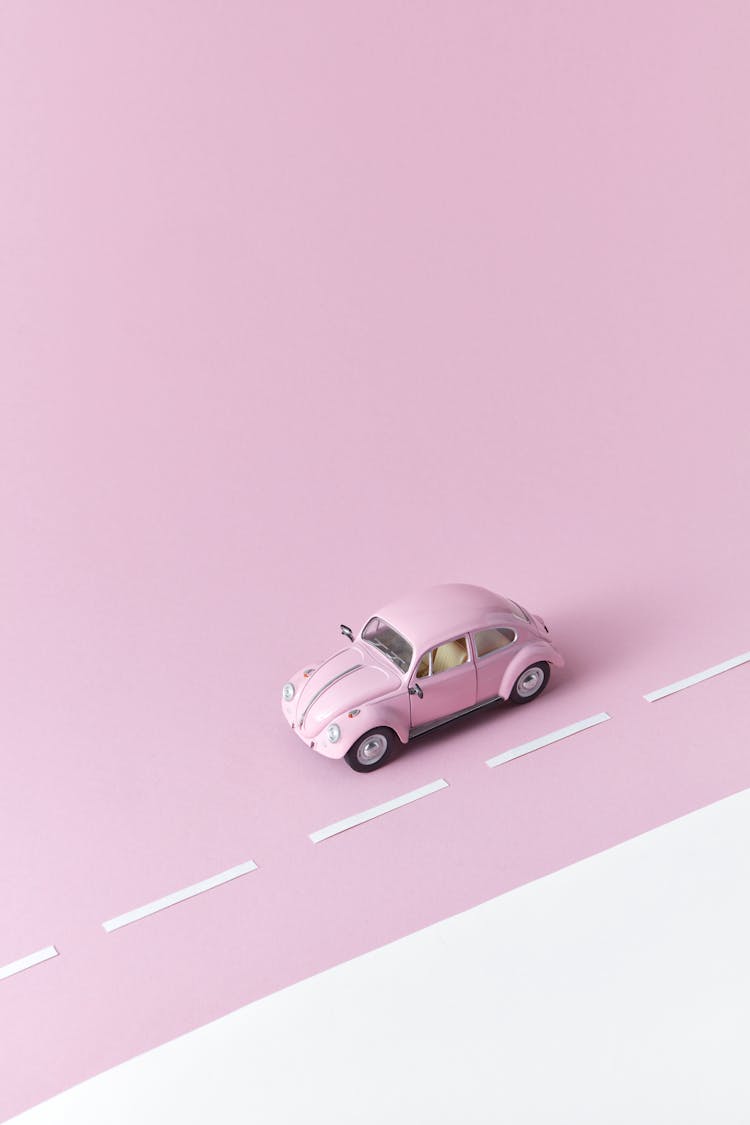 Photograph Of A Pink Miniature Car Beside White Paper Strips