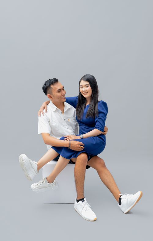 Free Asian couple sitting together with smiles in a minimalist studio setting. Stock Photo