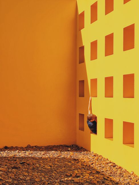 A child plays creatively on a sunny day against a vibrant orange wall with square cutouts.
