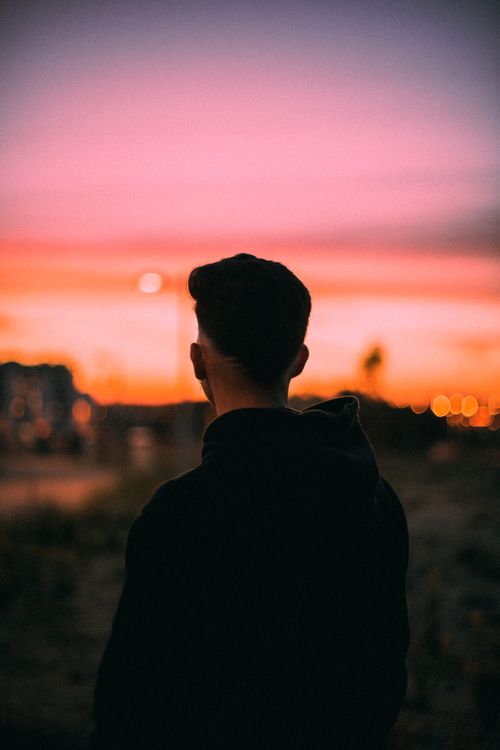 Free A person in a hoodie gazing at a vivid sunset, creating a serene silhouette scene. Stock Photo