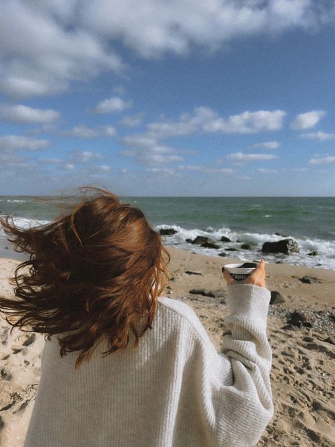 A woman with flying hair holds a drink by the shore on a windy day in Bilhorod-Dnistrovs'kyi, Ukraine.