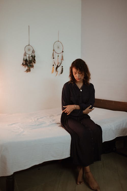 Woman Sitting on Bed with Dream Catchers on Wall