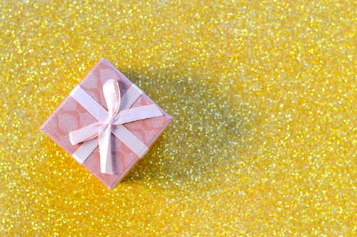 Pink Gift Box With Ribbon on Glittery Gold Surface