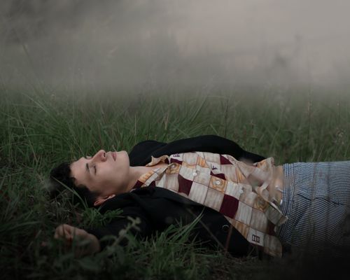 Free A man in a plaid shirt lies peacefully on grass, surrounded by fog. Stock Photo