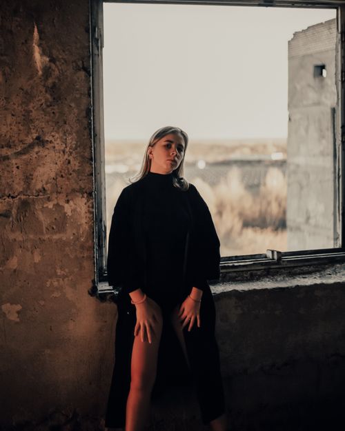 Free A woman stands in an abandoned building by a window, creating a mysterious atmosphere. Stock Photo