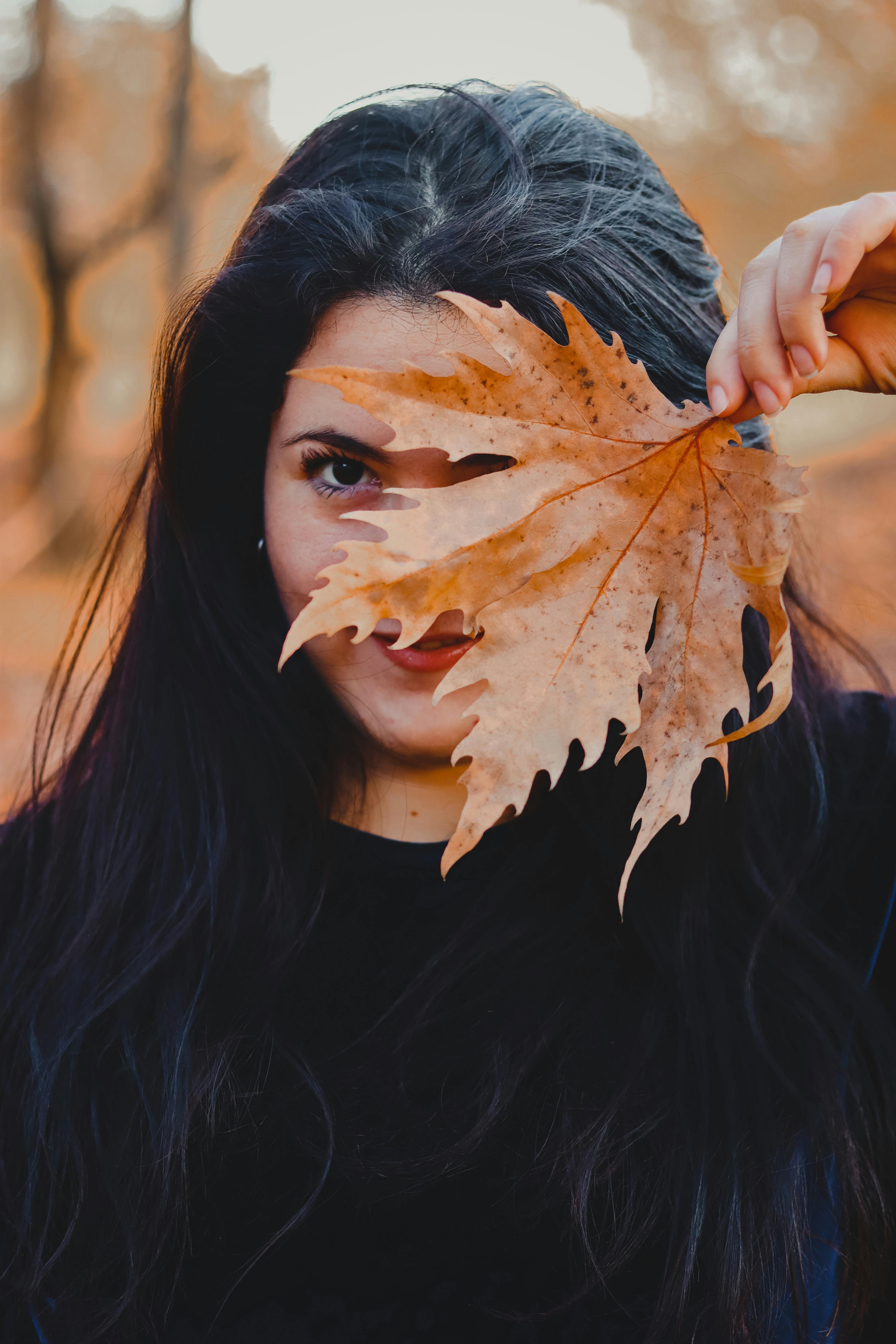 Portrait of a woman holding a dried leaf against her face, capturing an autumn vibe.