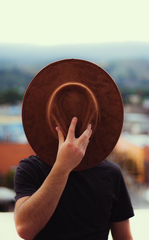 Free Person concealing face with a brown hat in an outdoor setting, creating an enigmatic vibe. Stock Photo