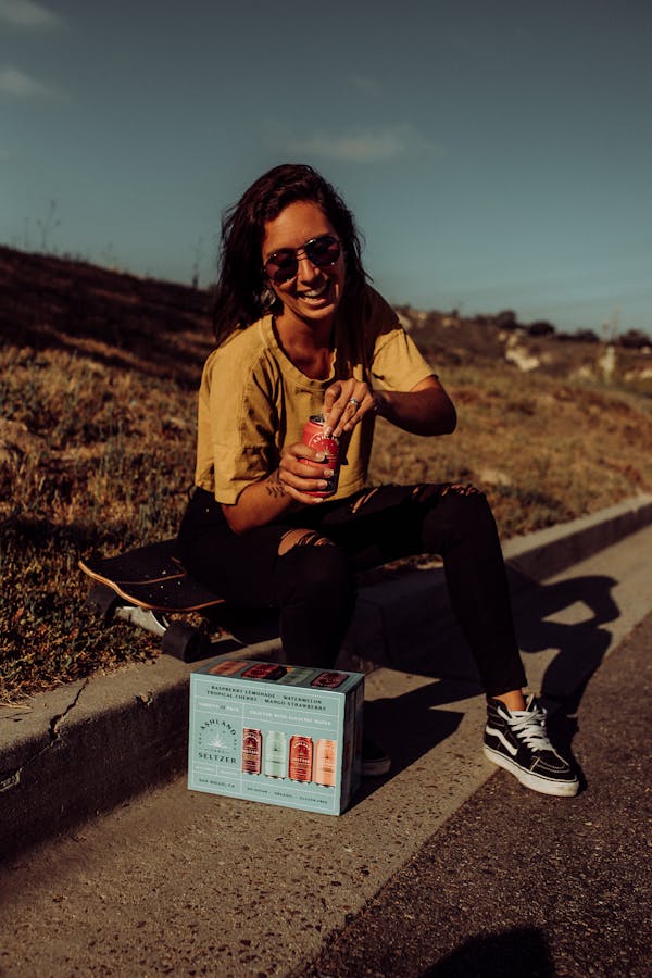 Woman Sitting on Roadside Opening a Can of Drink
