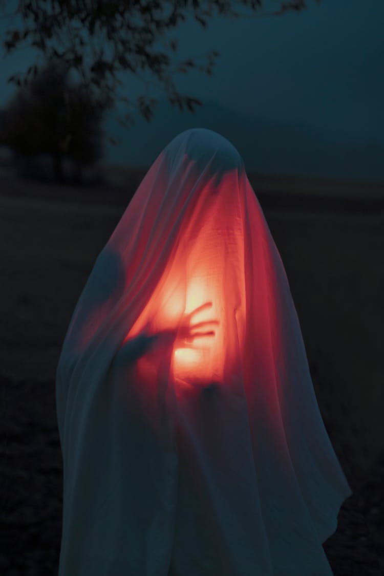 Unrecognizable Person Holding Lit Lamp Covered With Bed Sheet 