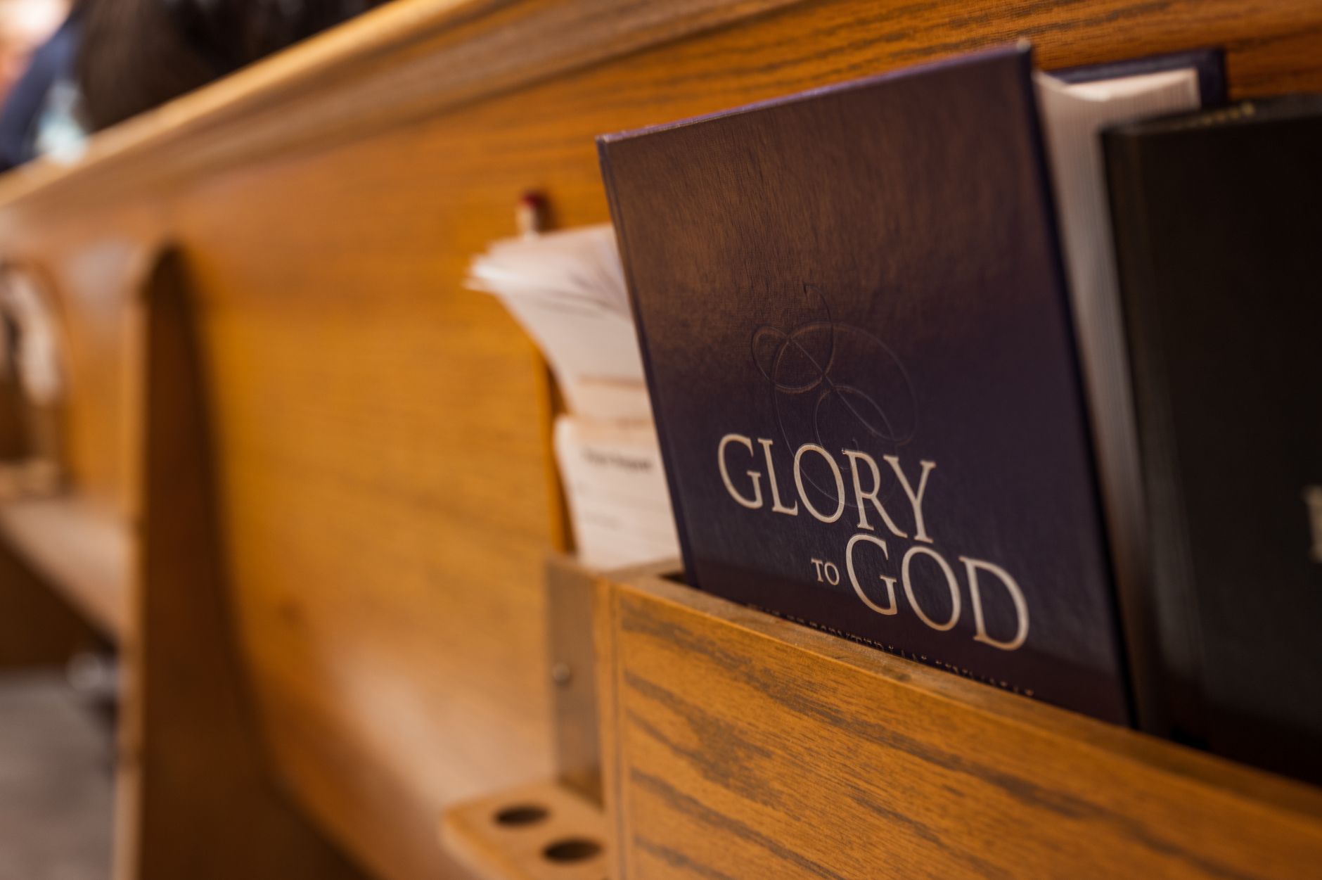 A hymnal titled 'Glory to God' placed in a church pew's book holder, capturing a religious atmosphere.