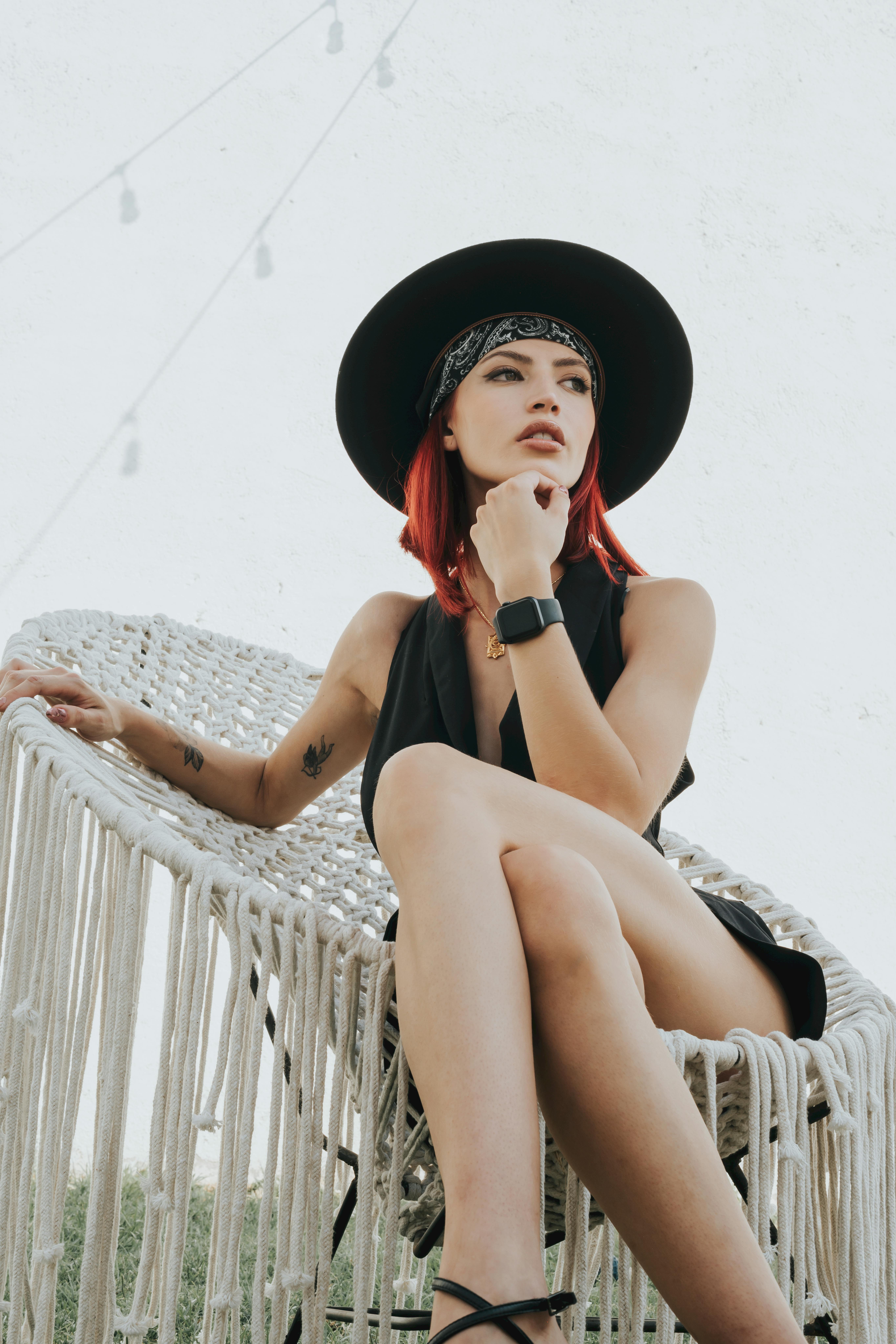 Fashionable woman in a black hat sitting stylishly in a woven chair. Modern and chic vibe.
