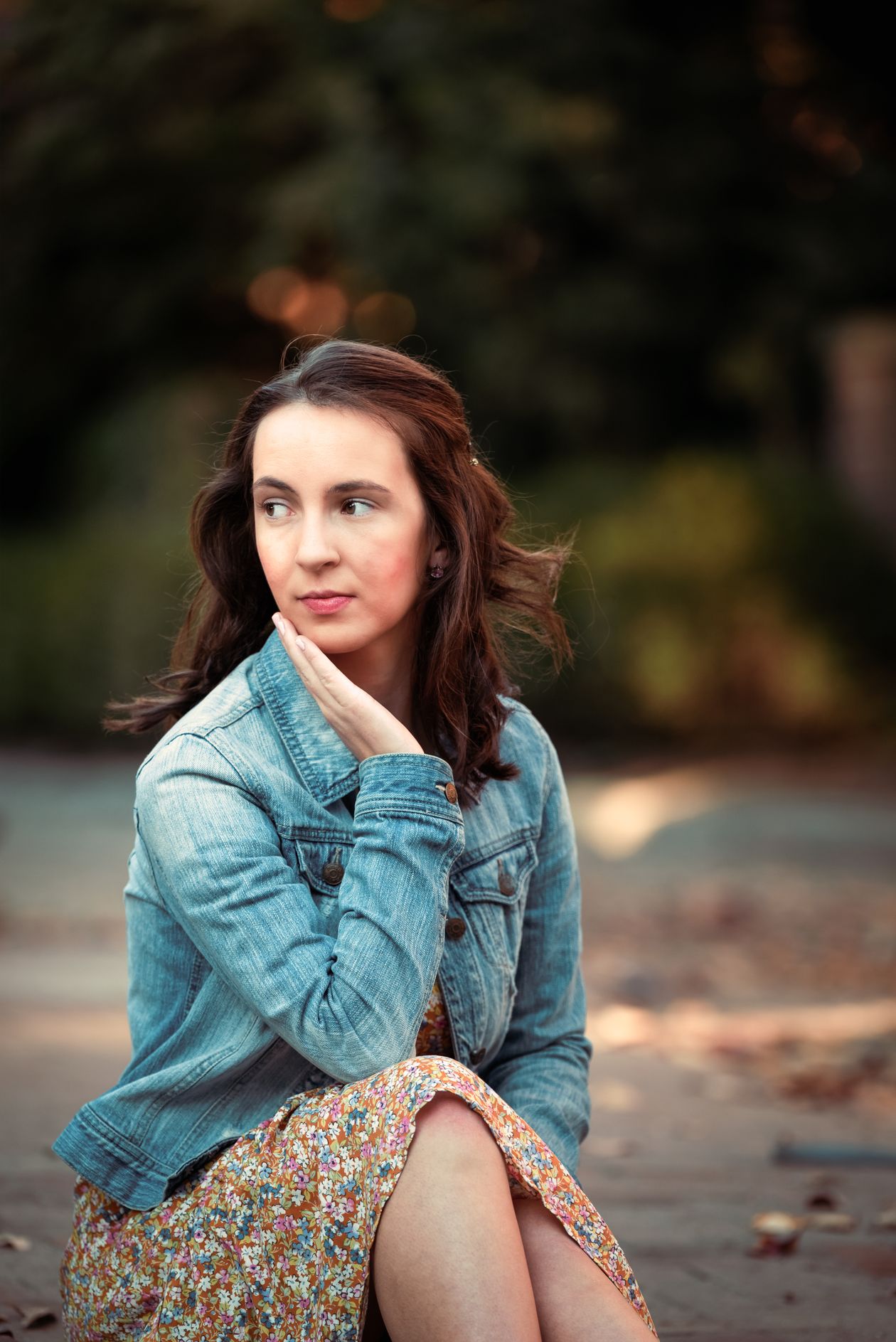 Woman in a denim jacket over a floral mini dress sitting outdoors