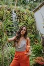 A Woman in Gray Tank Top and Orange Pants Standing Beside a Plant