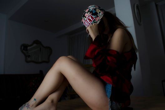 一位戴着花卉帽子、穿着休闲装的时尚年轻女性坐在室内，身上有纹身