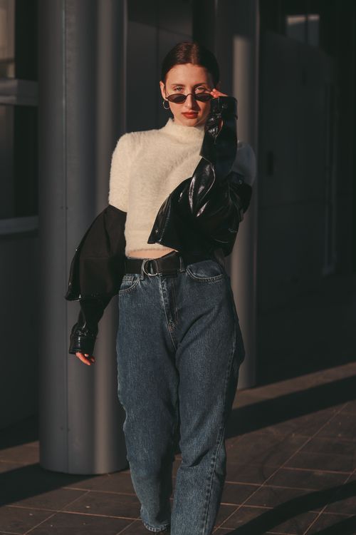 Free Stylish woman wearing sunglasses, oversized jacket, and jeans walking with confidence on a city street. Stock Photo