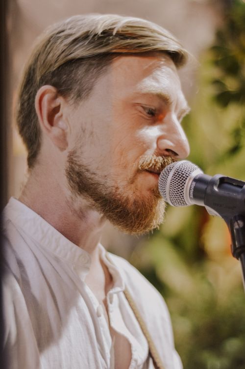 Free A male singer with a beard performing live outdoors with a microphone. Stock Photo