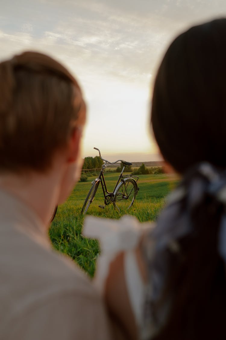 View From Behind Couple On Bicycle Standing In Green Meadow