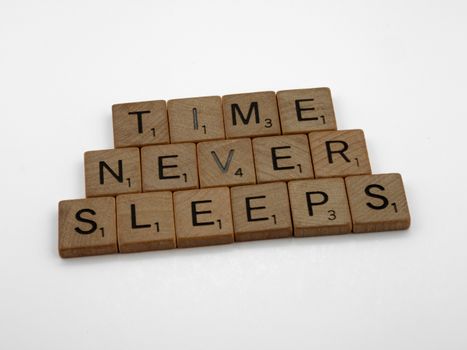 Wooden Scrabble tiles arranged to spell 'Time Never Sleeps' on a white background.