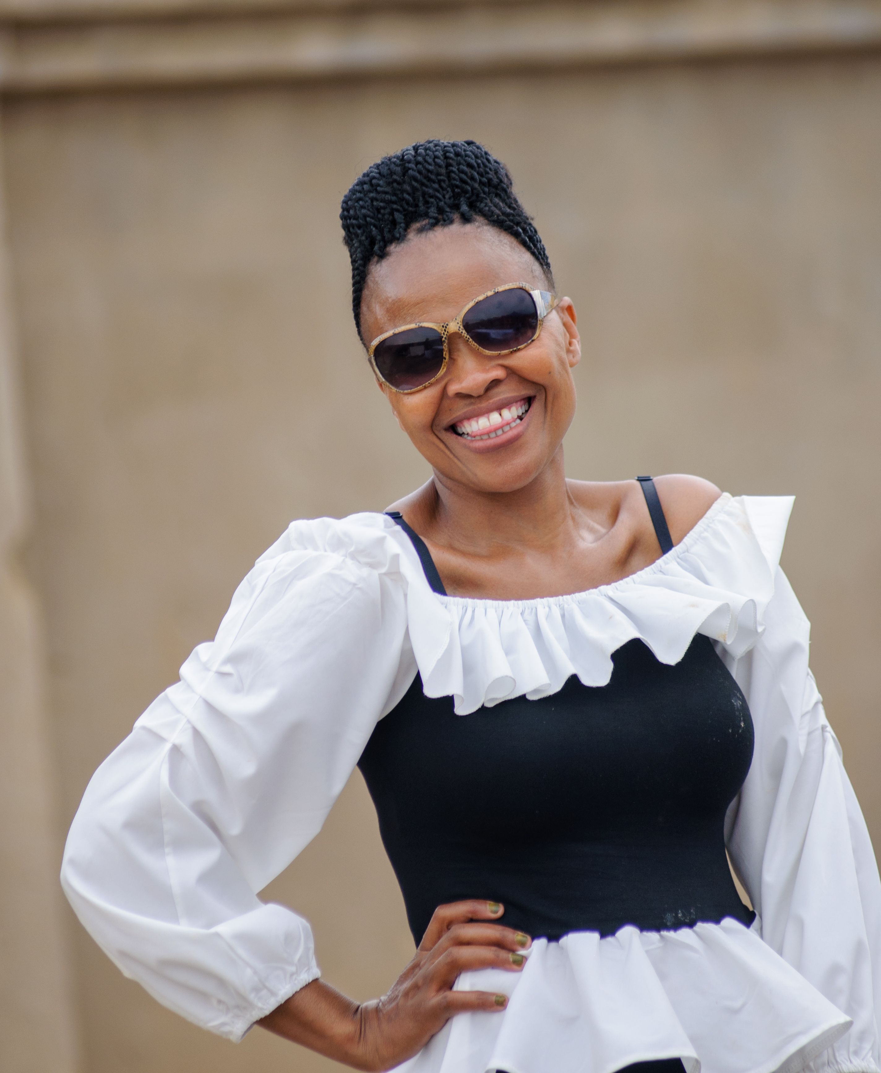 Portrait of a smiling woman in sunglasses wearing a trendy black and white outfit outdoors.