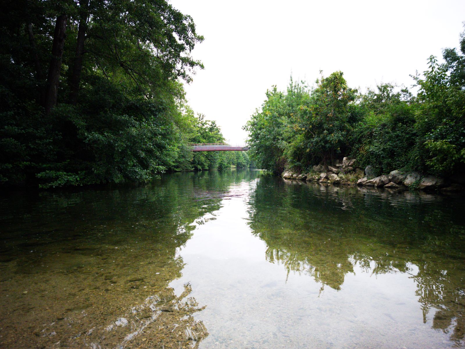 Rivière claire et peu profonde avec une passerelle et le reflet des arbres