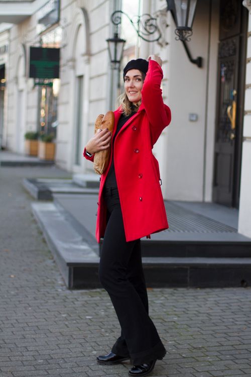 Free Smiling woman in red coat and beret holding a baguette on a stylish street. Stock Photo