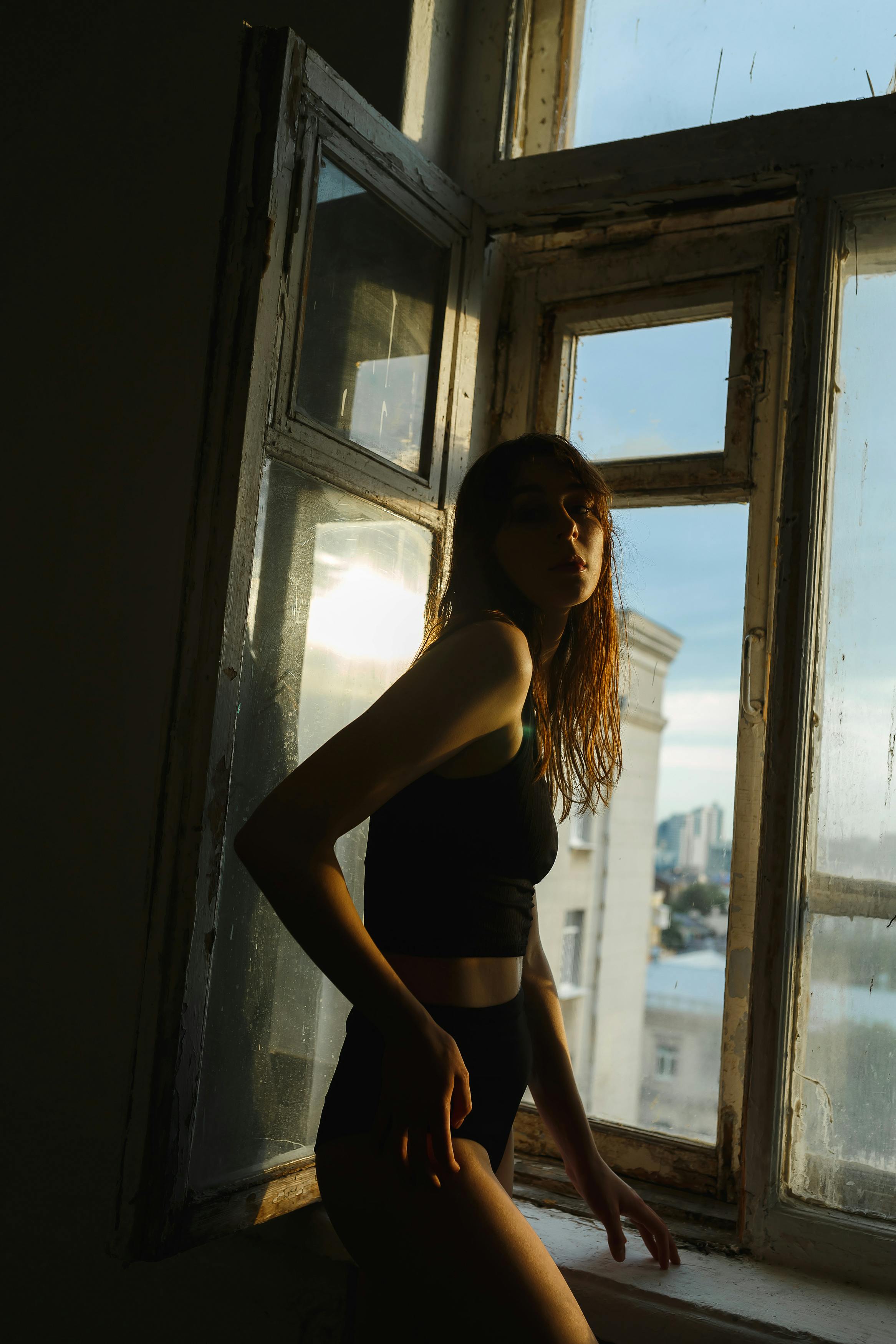 Artistic silhouette of a woman by an open window capturing moody ambient light.