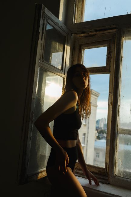 Artistic silhouette of a woman by an open window capturing moody ambient light.