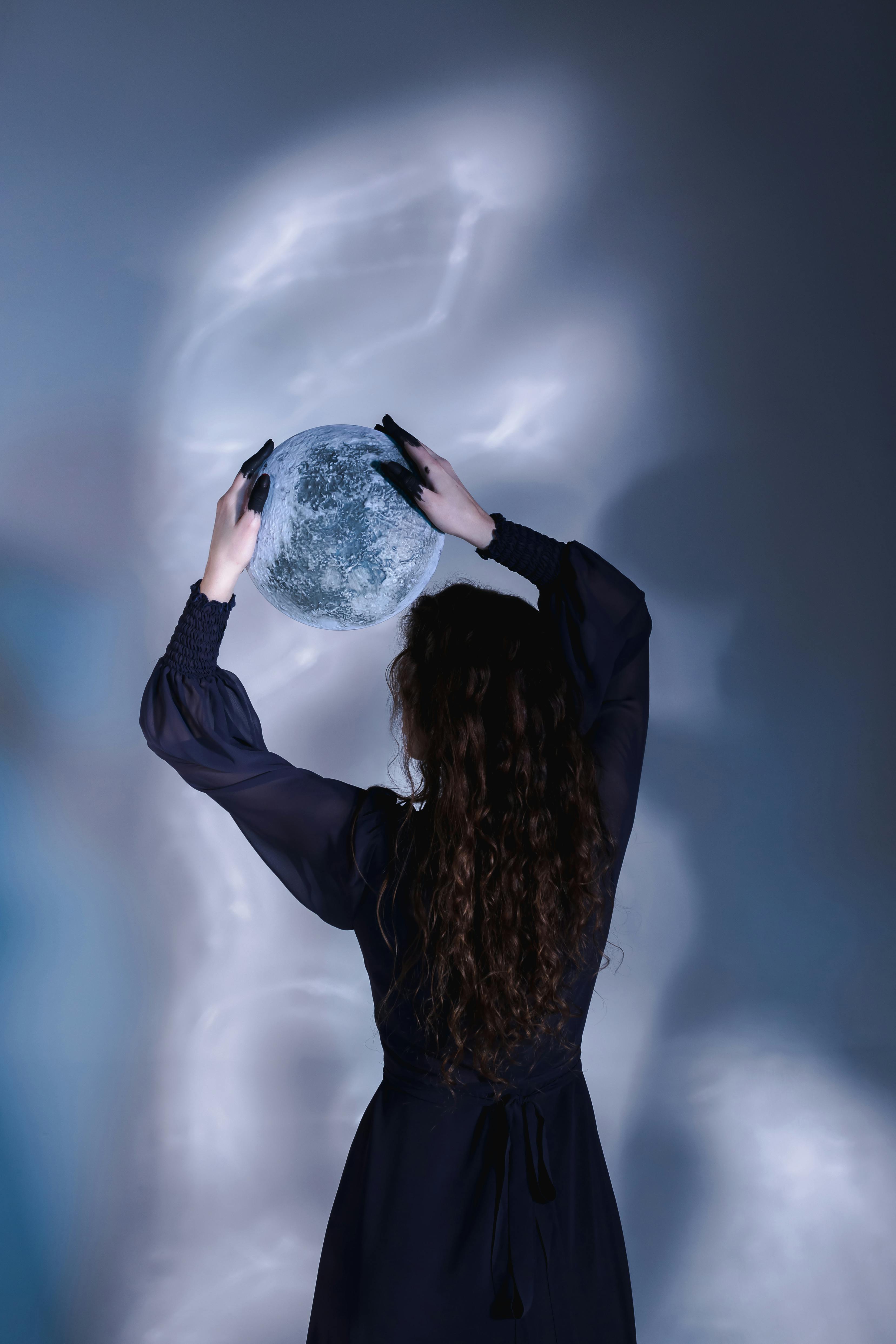 A woman in a black dress holds a glowing translucent sphere in a dark studio setting.