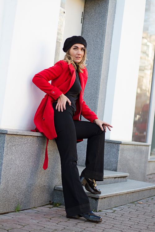 Free Stylish woman in a red coat and beret poses confidently against a building wall. Stock Photo