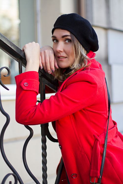 Free Chic young woman in red coat and black beret leaning on railing. Fashionable autumn look. Stock Photo