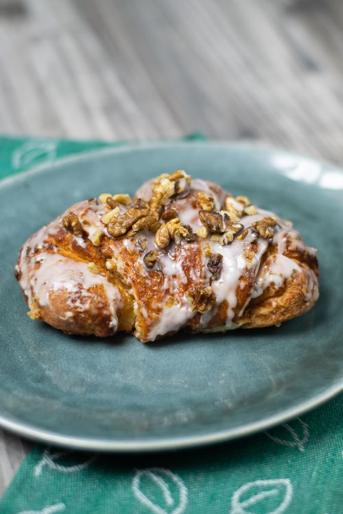 Free Appetizing croissant topped with walnuts and icing on a blue plate. Stock Photo
