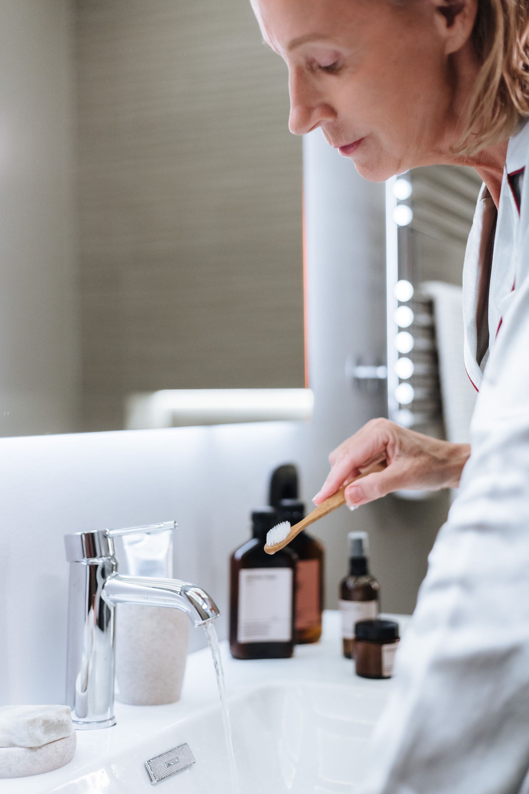 Older woman brushing her teeth in a well-lit bathroom during an independent morning care routine