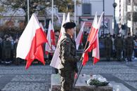 Military personnel in uniform hold national flags during an outdoor ceremonial event.