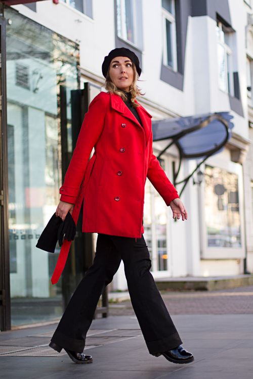 Free Stylish woman wearing a red coat walking confidently on a city street during winter. Stock Photo