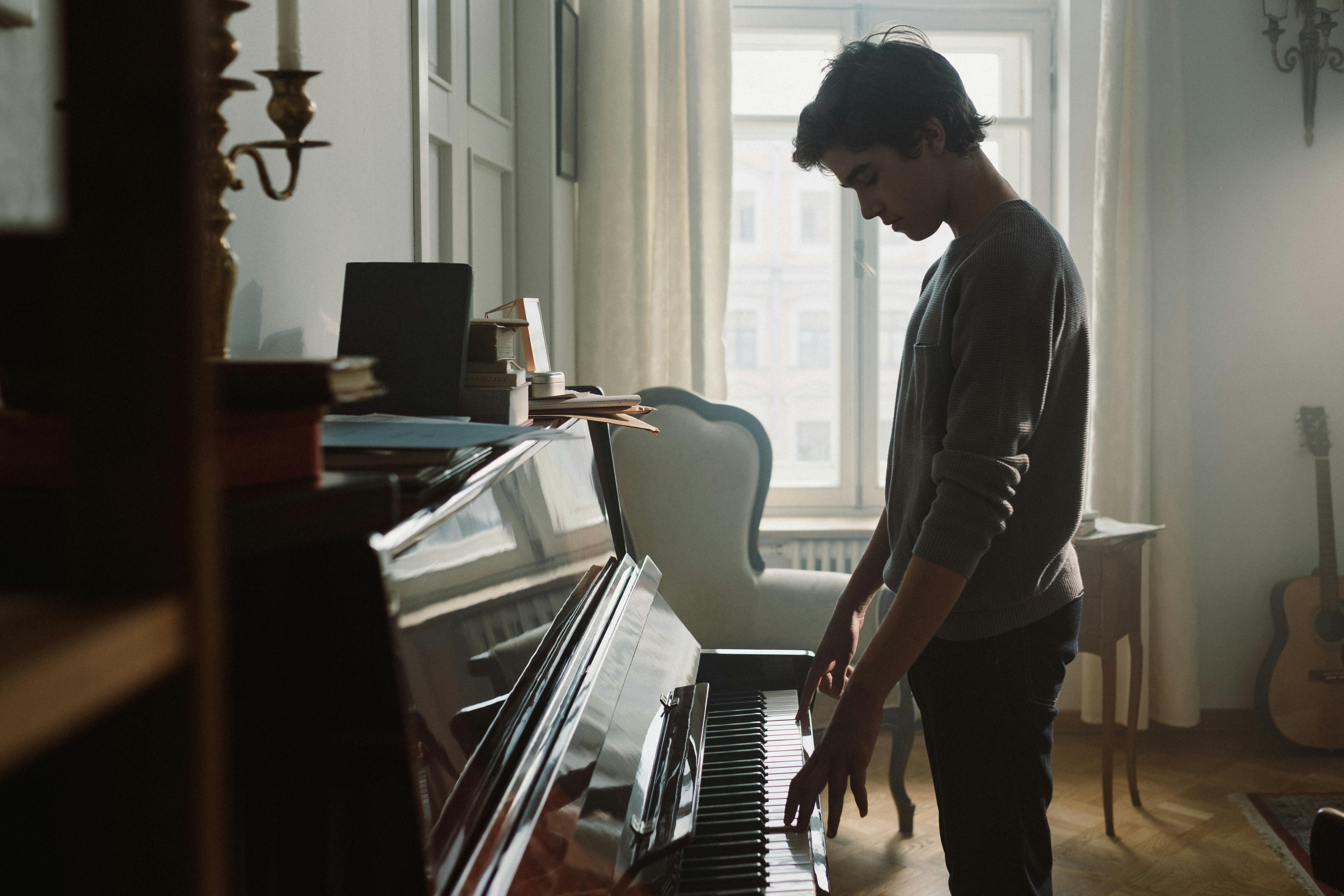 Free Teenage Boy Paying the Piano While Standing Near Window Stock Photo