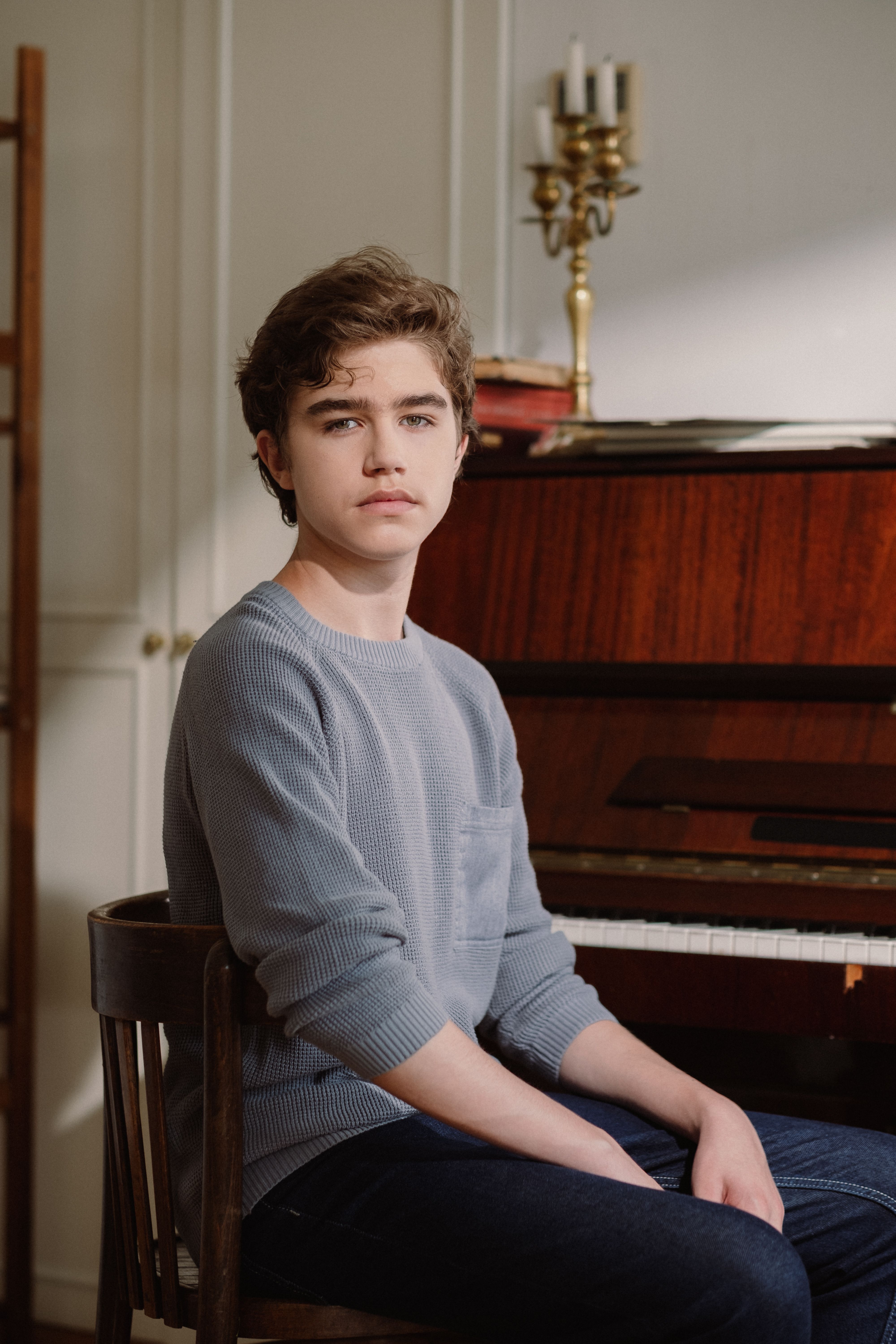 Portrait of a young boy sitting in front of a grand piano indoors, looking thoughtful.