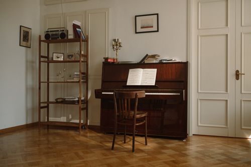 Free Warm, inviting room with an upright piano, wooden chair, and vintage decor, perfect for music lovers. Stock Photo