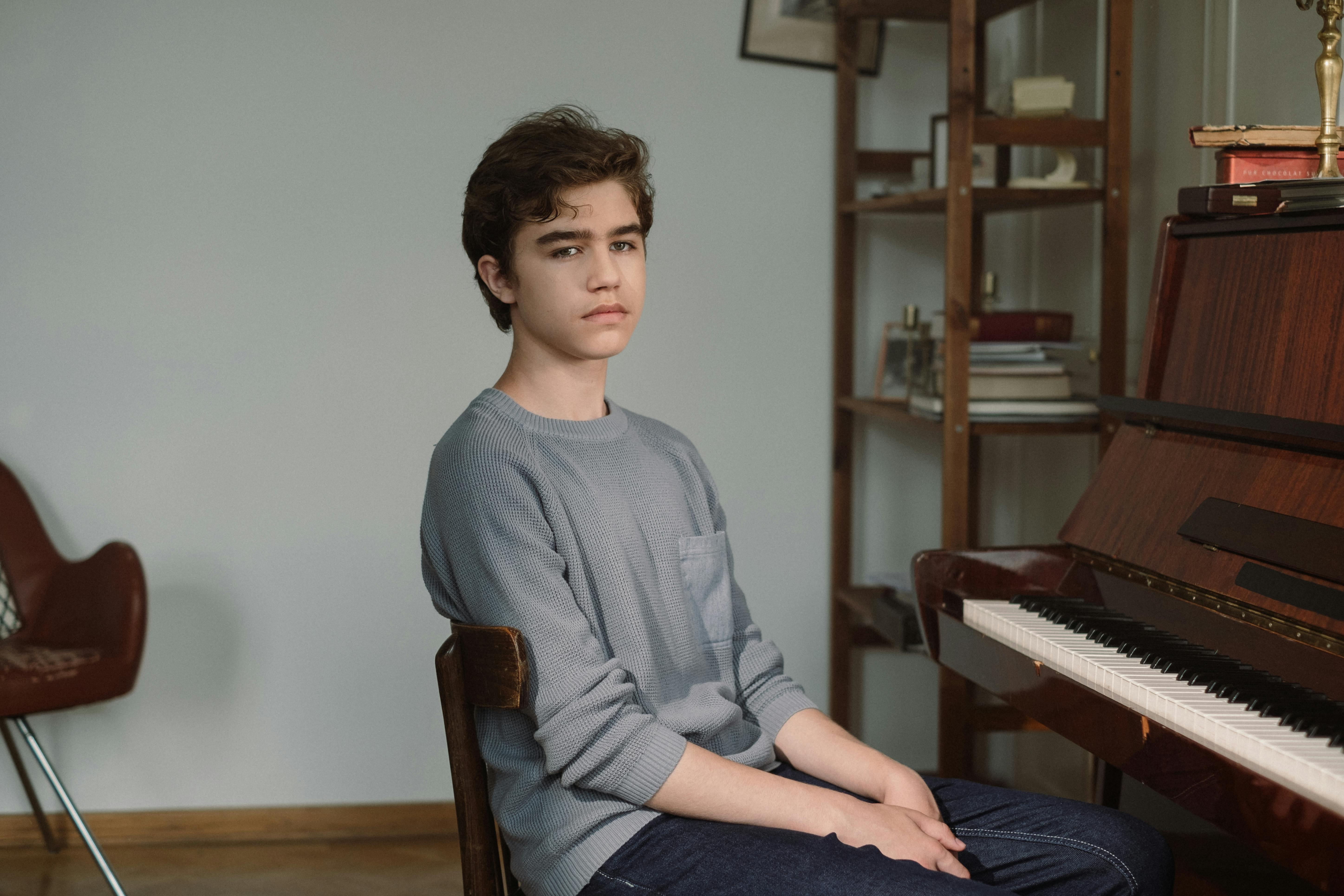 boy sitting on wooden chair near a piano