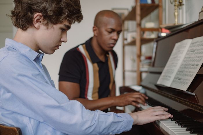 Profesor îndrumând un elev adolescent la pian