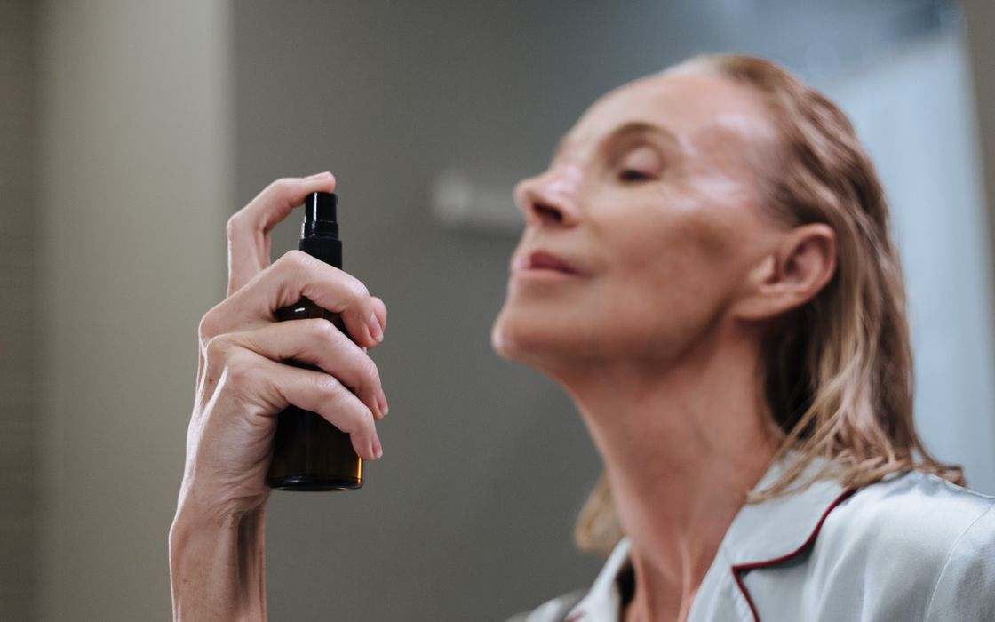 Senior woman demonstrating daily skincare routine, spraying face with a beauty product.