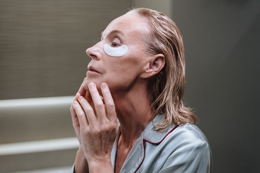 An elderly woman with blond hair applying eye patches as part of her morning skincare routine.