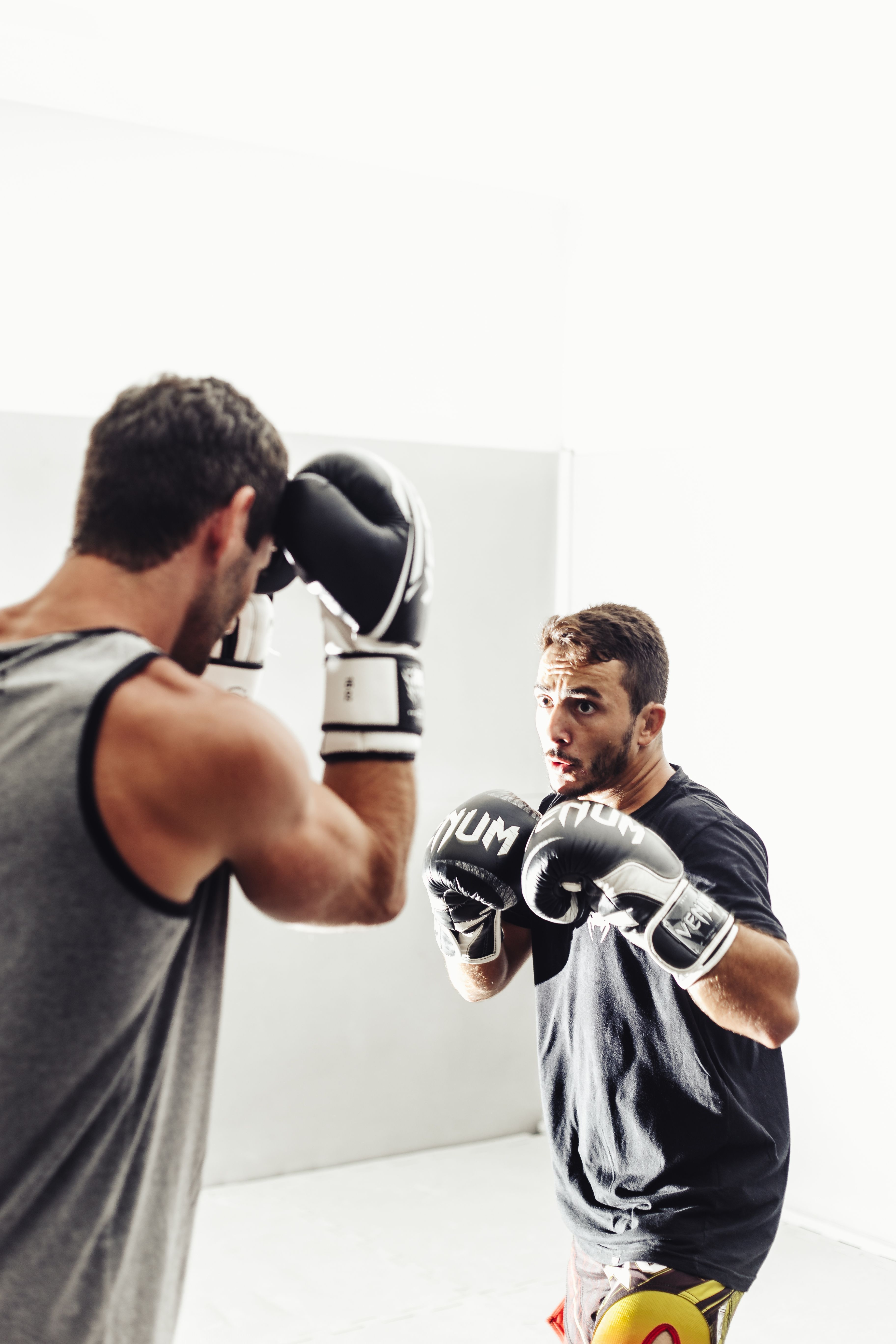 Two men in boxing practice indoors with focused expressions and gloves.