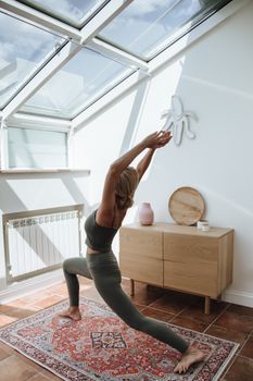 A woman performs yoga in a sunlit attic with a skylight, enhancing fitness and mindfulness.